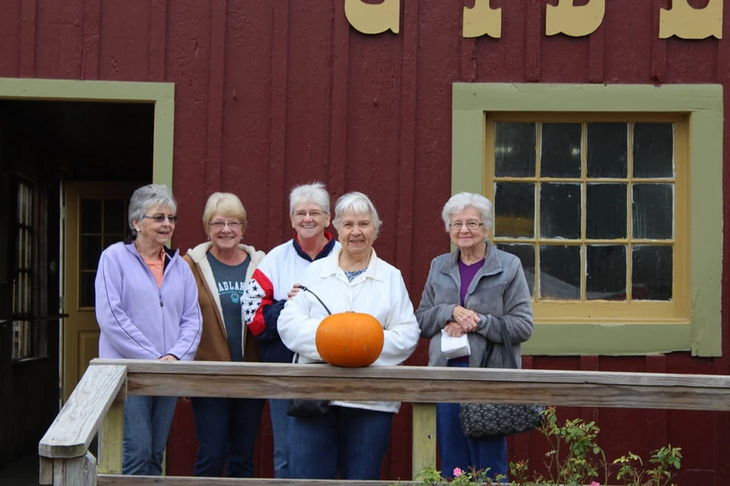 A group from Piper Bible Church’s 55 and Alive fellowship on an outing, standing together outside a red wooden building.